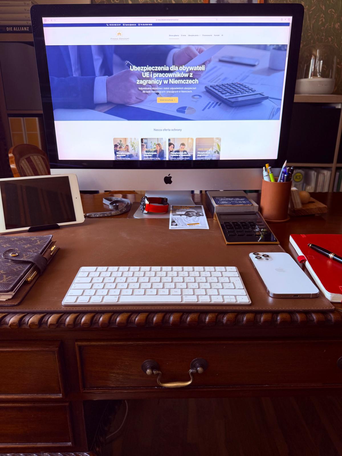 Biurko z komputerem iMac wyświetlającym polską stronę Ubezpieczenia w Niemczech